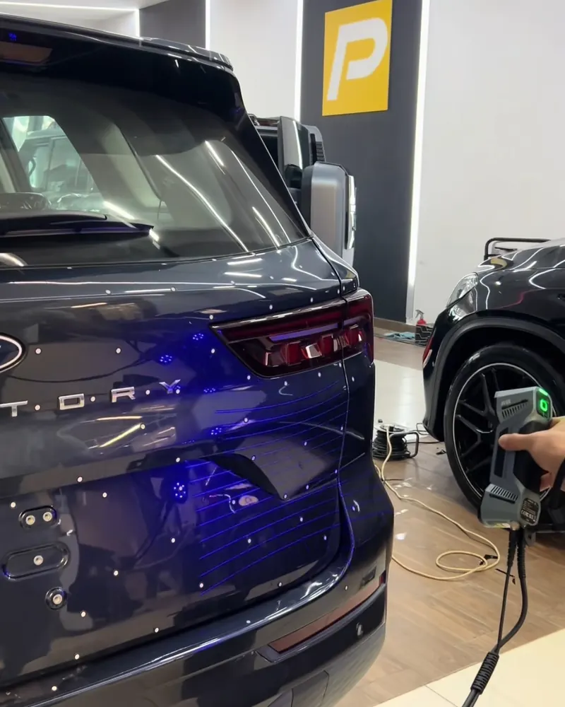 فني يمسح الباب الخلفي لسيارة بجهاز المسح الليزري ثلاثي الأبعاد داخل معرض PROF Car Care، وخطوط الليزر الزرقاء ظاهرة على الهيكل